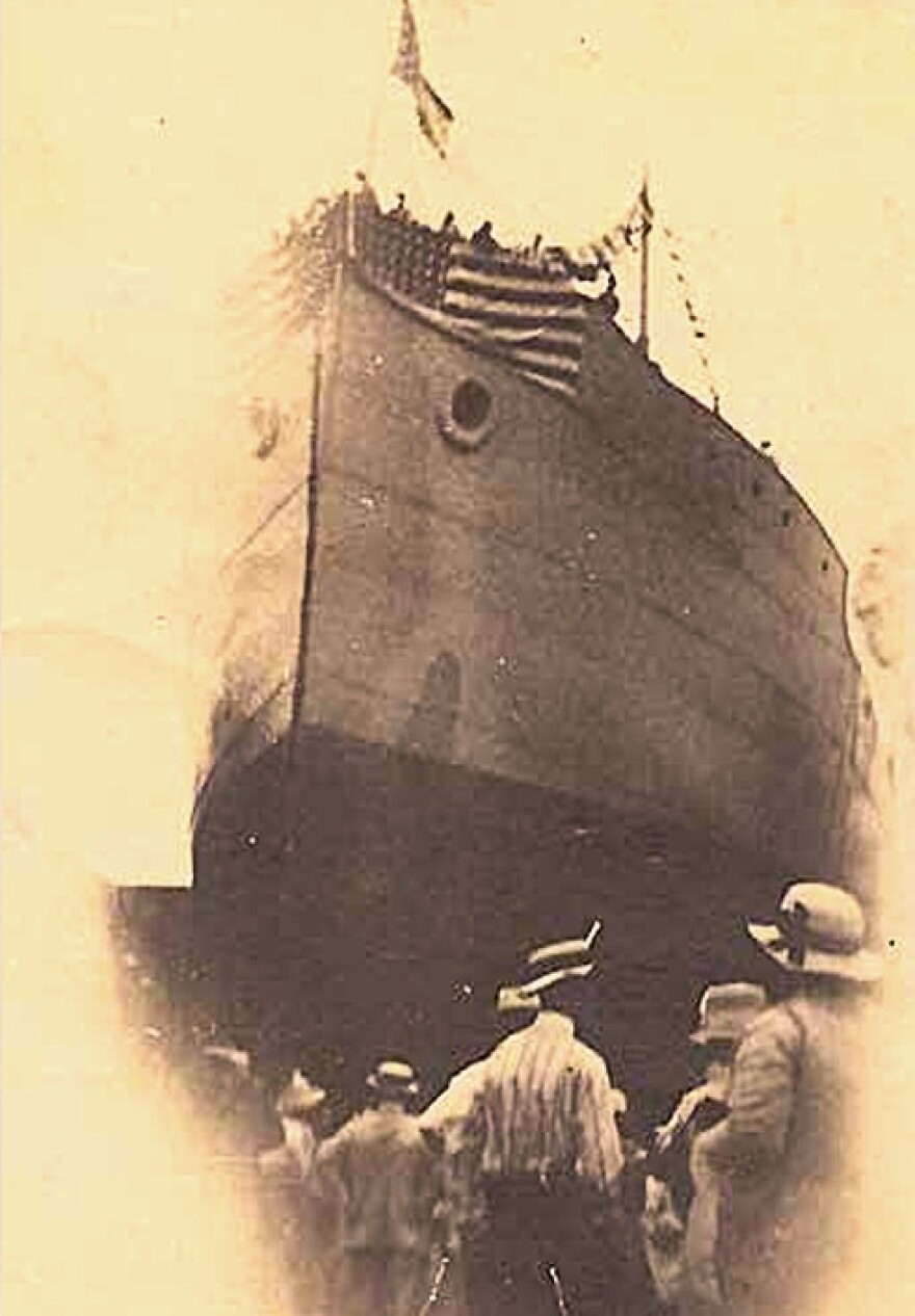 old B&W image of a large ship with people on the dock in front of it