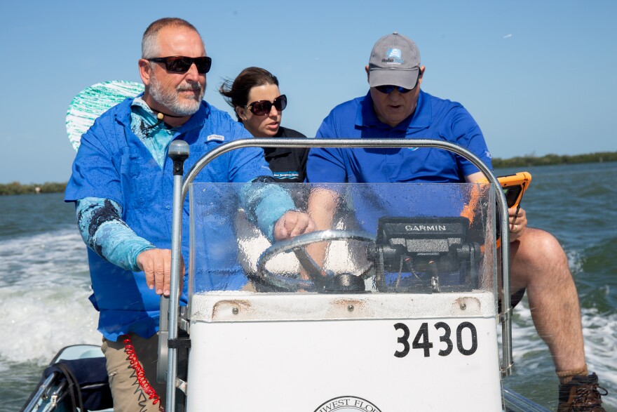 Two men in blue shirts and a woman in black on board a small boat going through water and leaving white trails behind them. All three are wearing sunglasses. 
