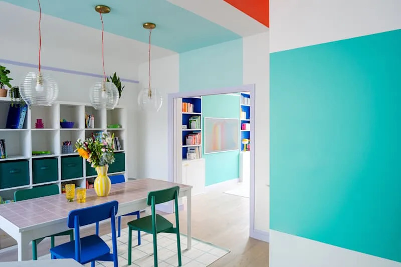 Bright dining area featuring a table with colorful chairs, pendant lights, and vibrant wall colors.