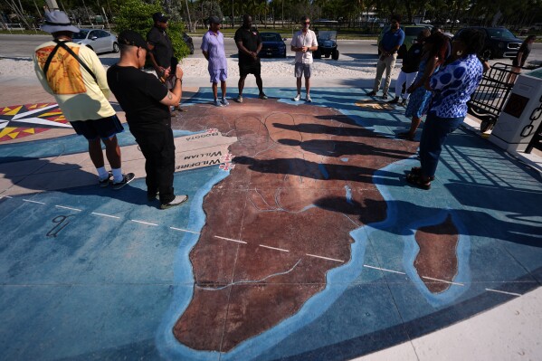 Corey Malcom, center, lead historian with the Florida Keys History Center, talks to Black divers from the Underwater Adventure Seekers, as they visit a memorial built on the site where hundreds of Africans who died in 1860 after being rescued from three slave ships were buried, on Higgs Beach in Key West, Fla., Saturday, May 9, 2026. (AP Photo/Rebecca Blackwell)