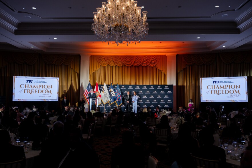 Adam Smith Center Founding Director Carlos Diaz-Rosillo and FIU Preisdent Jeanette Nuñez at a fundraising event at Trump National Doral on May 16th, 2026. Banners on either side of the stage say "Champion of Freedom."