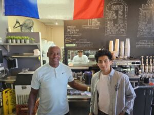 two men standing in a kitchen below a French flag