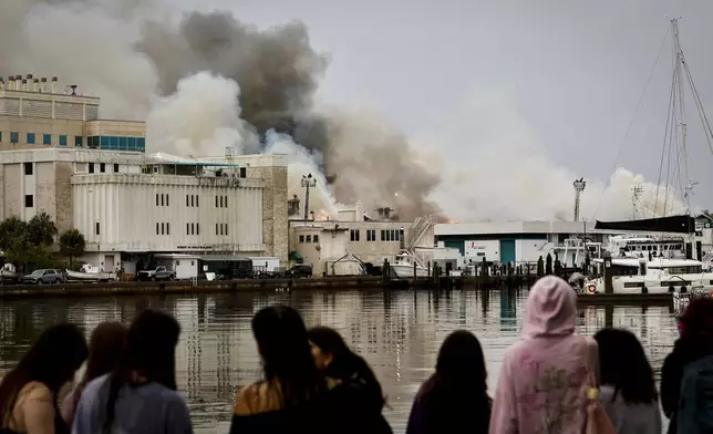 Onlookers watch as firefighters work to extinguish a fire at the University of South Florida campus Saturday, May 2, 2026, in St. Petersburg, Fla. (Luis Santana/Tampa Bay Times via AP)