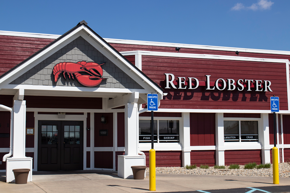 Front exterior of a Red Lobster restaurant in Indianapolis, Indiana with front doors, windows, and two handicapped parking spots, against a blue sky