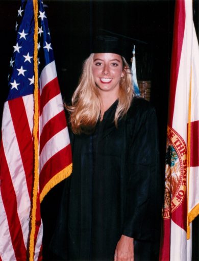 Sara Blakely stands in a black graduation robe beside the American flag and the State of Florida flag. The photo was taken May 1, 1993.