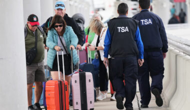 FILE - Travelers walk with their luggage past TSA agents at Fort Lauderdale-Hollywood International...