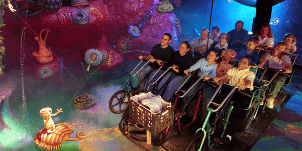 People riding a dynamic simulation ride with underwater-themed decorations including colorful coral and a character on bicycles inside of E.T. Adventure at Universal Studios Florida.