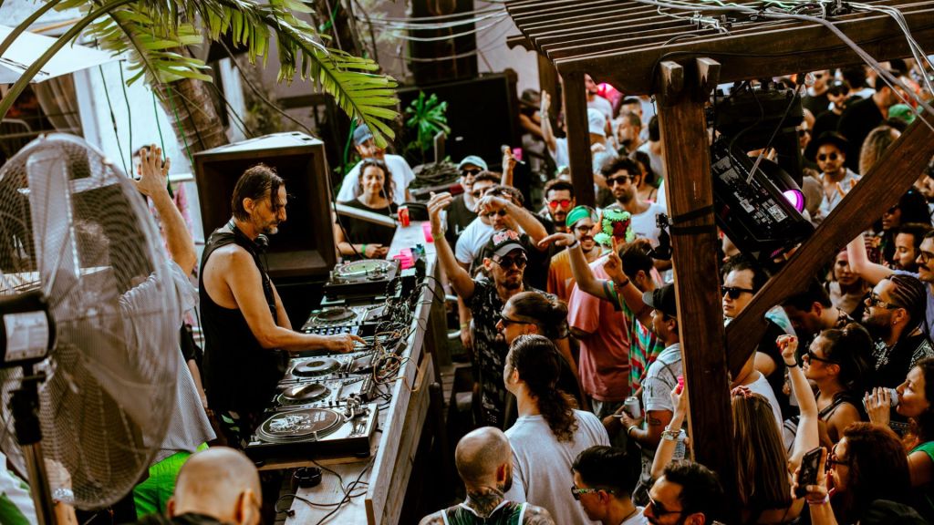 Photo of a DJ performing under a tent in front of a crowd. 