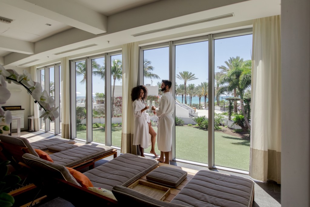 photo of a man and woman in robes in front of floor-to-ceiling windows in front of a patio
