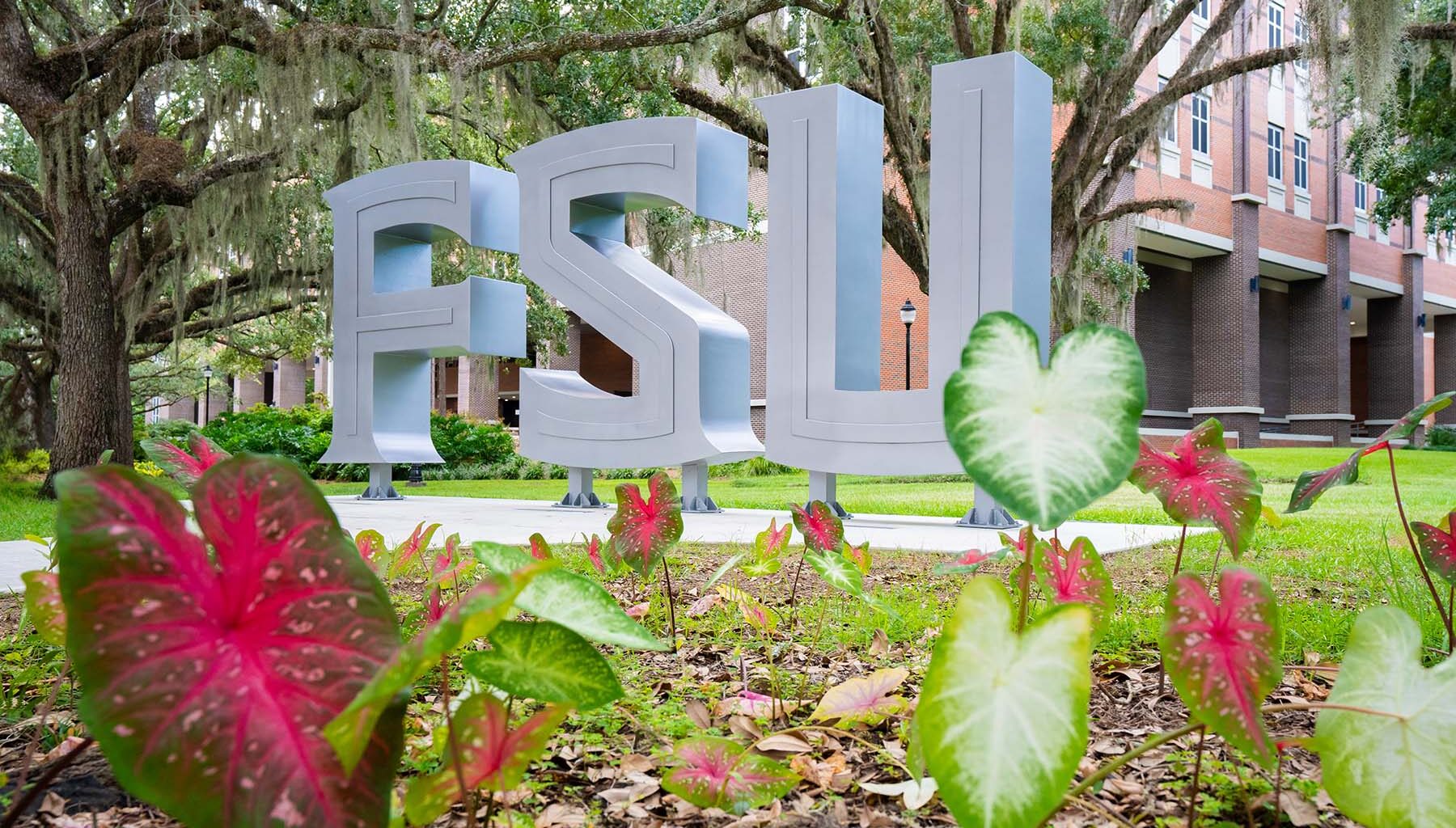Large silver “FSU” letters stand on a landscaped campus lawn