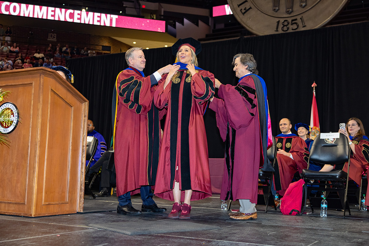 Sara Blakely stands on stage as an honorary hood is placed over her shoulders by President Richard McCullough and Provost Jim Clark.
