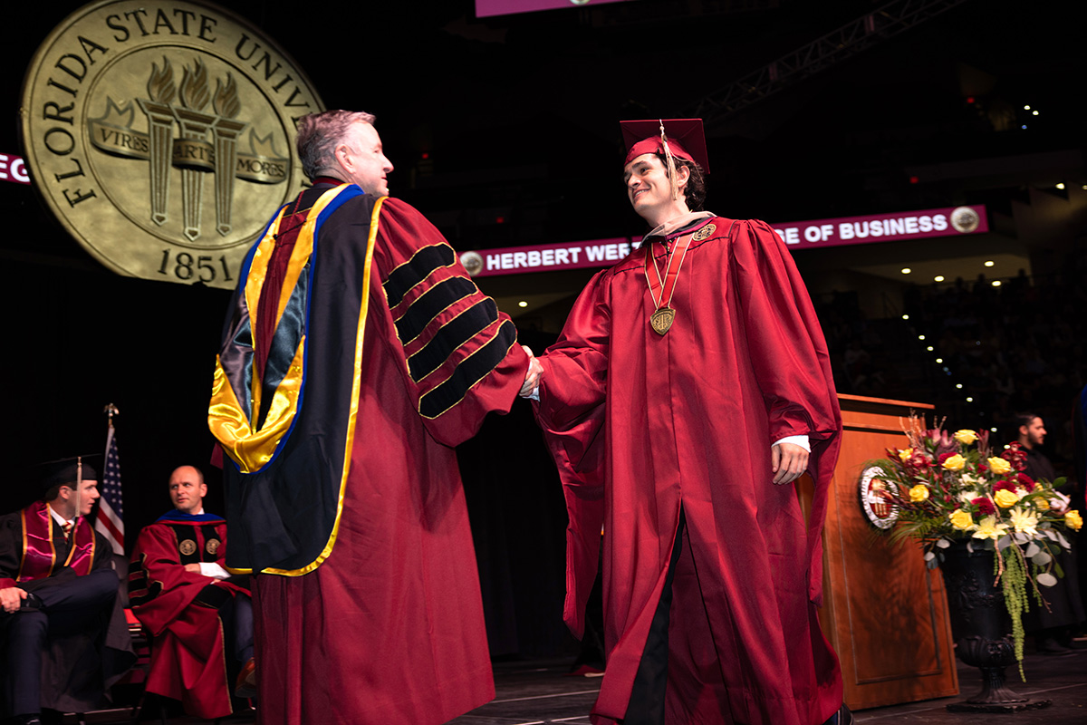 Graduates walk across the stage in garnet and black regalia during the Herbert Wertheim College of Business commencement ceremony at Florida State University.