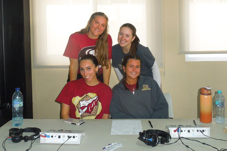 Four female students smiling with audiology equipment on a table in front of them.