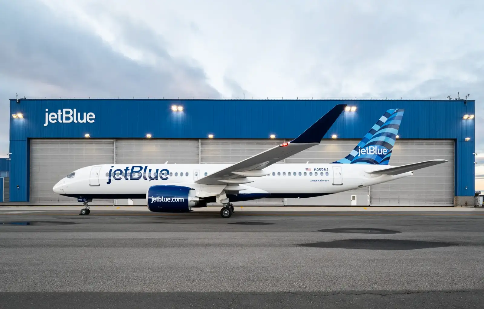 JetBlue Airbus A220-300 aircraft parked in front of blue hangar at airport