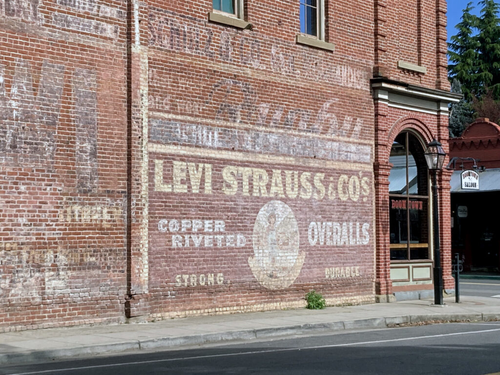This Levi Strauss & Co. “ghost” sign on a weathered brick wall in downtown Jacksonville reflects the town’s roots as a bustling commercial hub for Southern Oregon during the gold rush era. The sign was hand-painted by itinerant painters known as “wall dogs.” The paint’s survival is due to the high lead content, which made it durable but shortened the painters’ lifespans. Photo: Jim Flint.