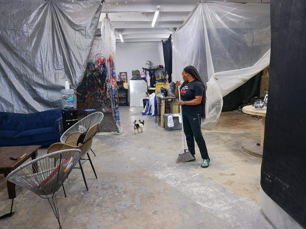 Christina Brown, 40, owner of The Break Room Miami, sweeps the hallway between the business's two rage rooms as her dog searches for a ball, Thursday, May 7, 2026, in Miami, Florida.