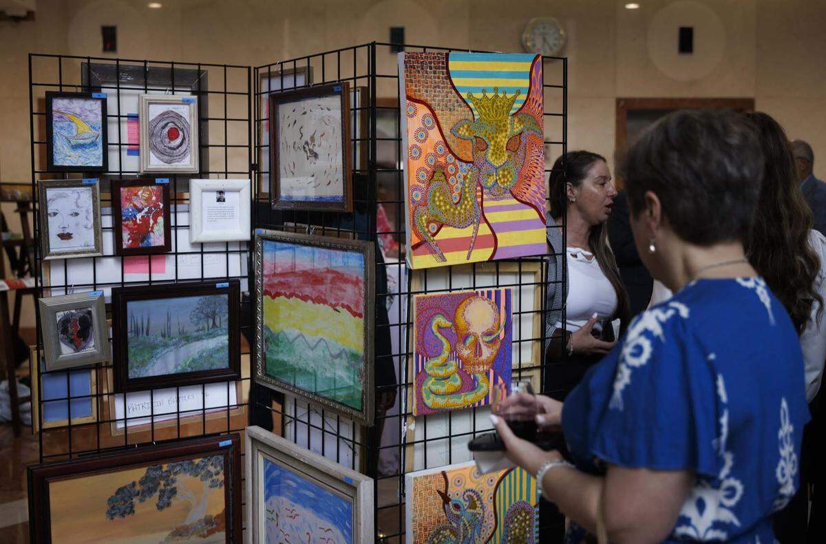 People look at artwork created by Oscar and other Camillus House artists during the Camillus House art show on Wednesday, May 27, 2026, in the foyer at Amerant Bank in Coral Gables, Fla.