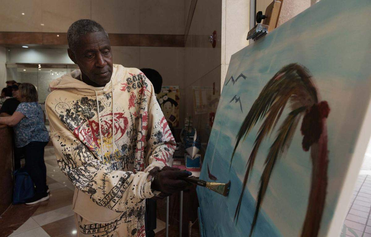 Barry Glenn, stroke survivor and artist, paints during the Camillus House art show on Wednesday, May 27, 2026, in the foyer at Amerant Bank in Coral Gables, Fla. Glenn says painting has helped him physically after his stroke but also mentally. “It's more of a therapy to see what can come of doing all this art,” said Glenn. 