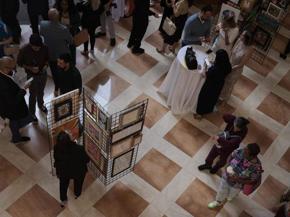 Patricia Battles, artist, right, and others walk through the Camillus House art show on Wednesday, May 27, 2026, in the foyer at Amerant Bank in Coral Gables, Fla.