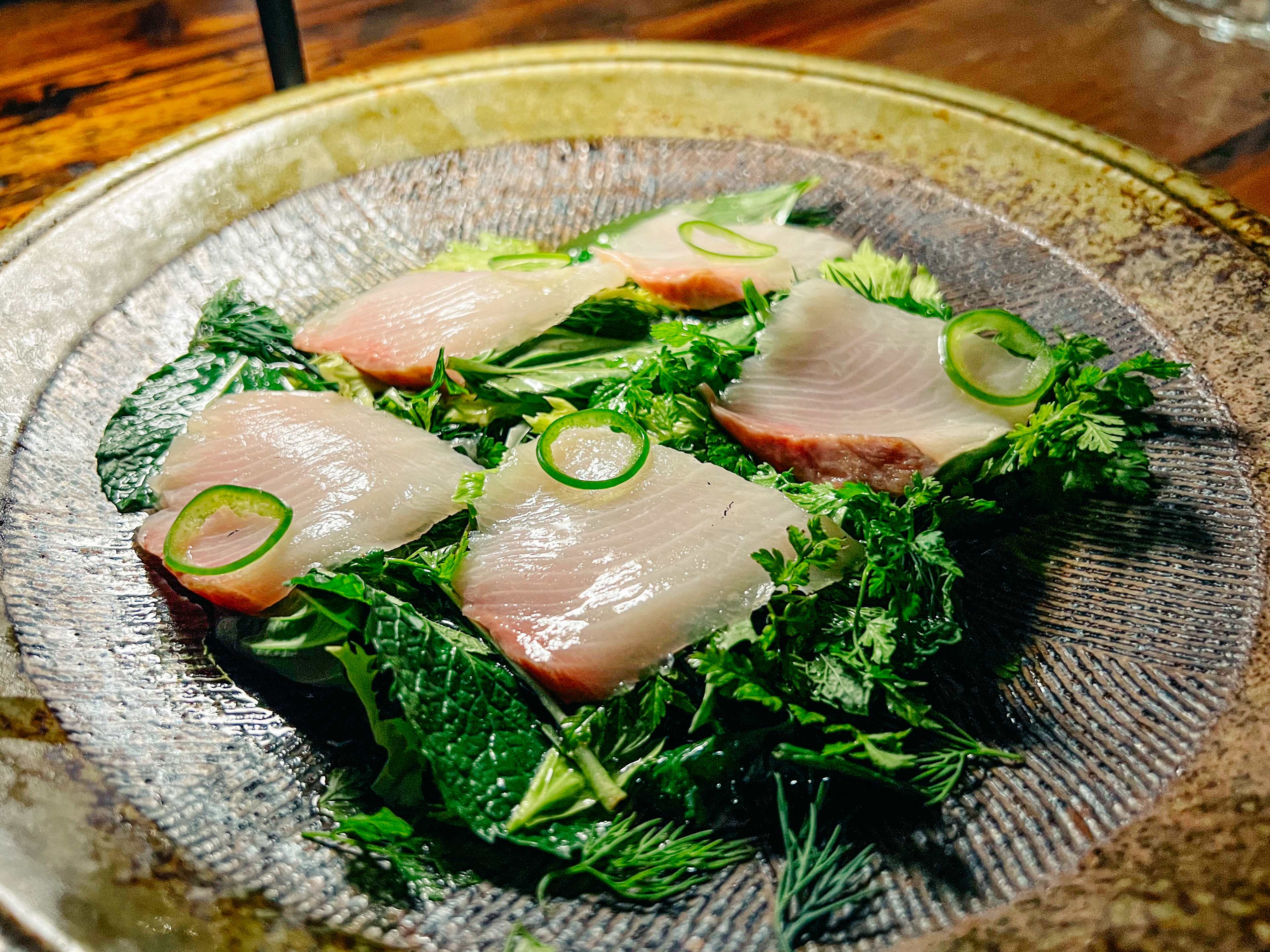 Slices of hamachi over herbs.
