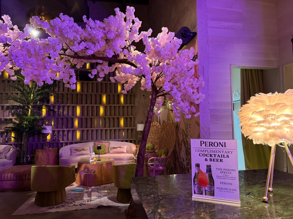 photo of a bar with cherry-blossom tree decor above a couch and a sign at the bar advertising complimentary Peroni beer and cocktails
