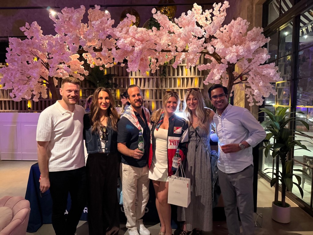 Photo of six men and women posing inside a bar beneath a decorative cherry-blossom tree