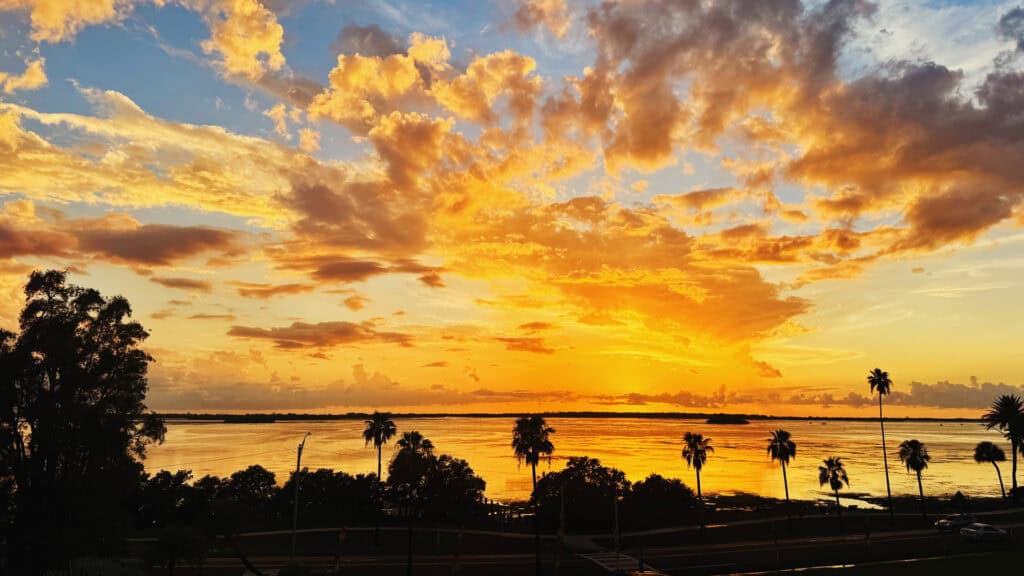 a vibrant cloud filled sunset of color - yellow, orange, and red clouds reflect over the water