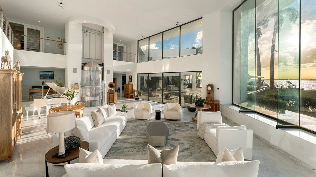 Spacious living room with glass elevator and modern seating in waterfront mansion