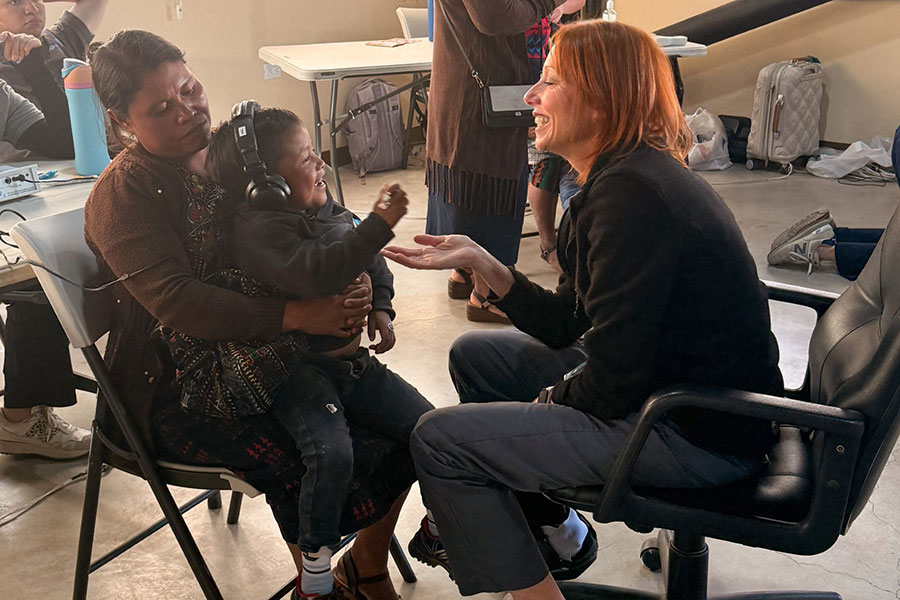 A woman conducts a hearing test on a baby sitting on its mother's lap.