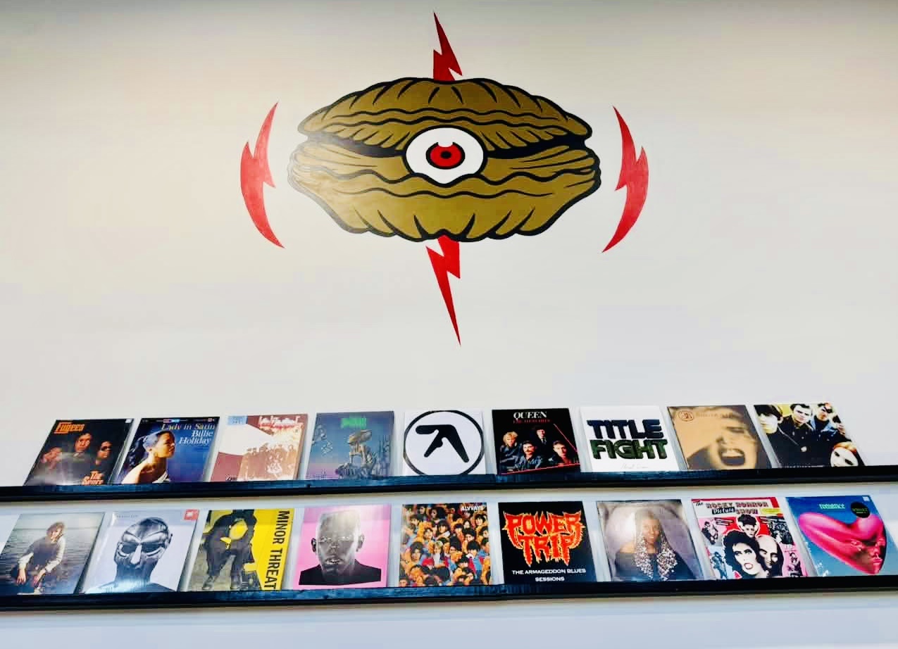 Photo of a wall with a shell-shaped logo and vinyl records.