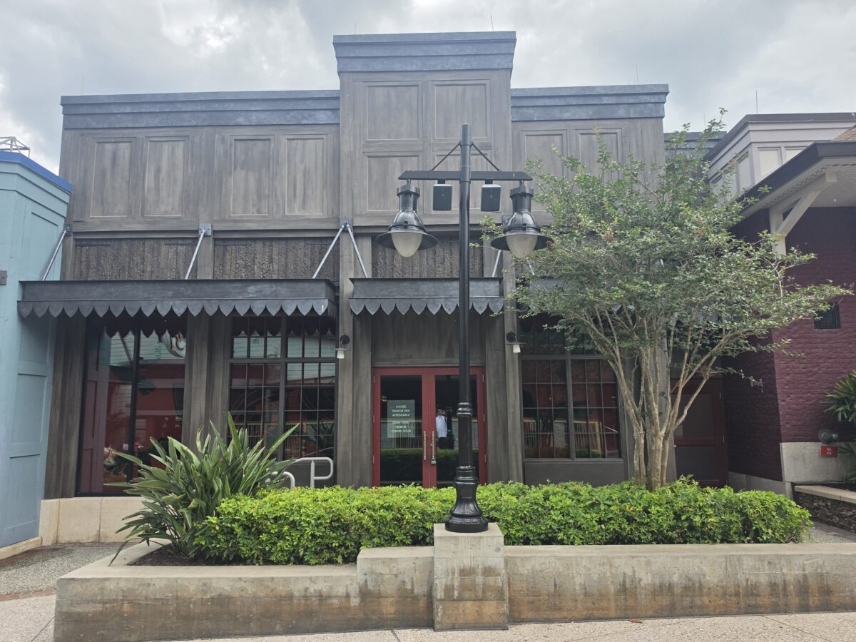 A wide view of the dark, gothic-style Six Ravens Disney Springs restaurant exterior between adjacent shopping district buildings under an overcast sky.
