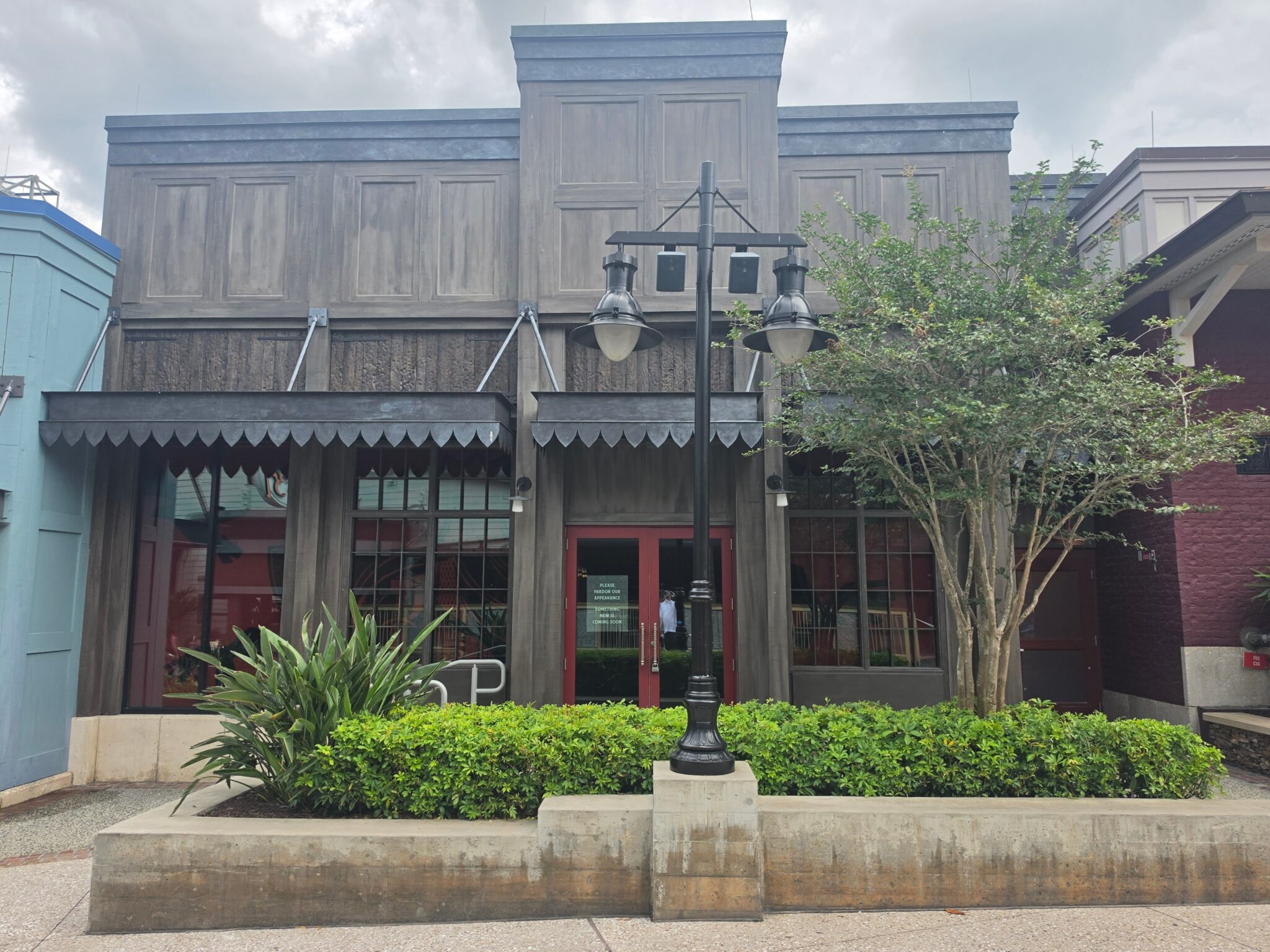 The dark wooden storefront facade of Six Ravens Disney Springs in May 2026, featuring red double entry doors, window panes, and a black street lamp in front.