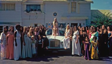 photo depicting a crowd of women around a Rolls-Royce. A woman sits on the car holding a poster depicting a cult leader