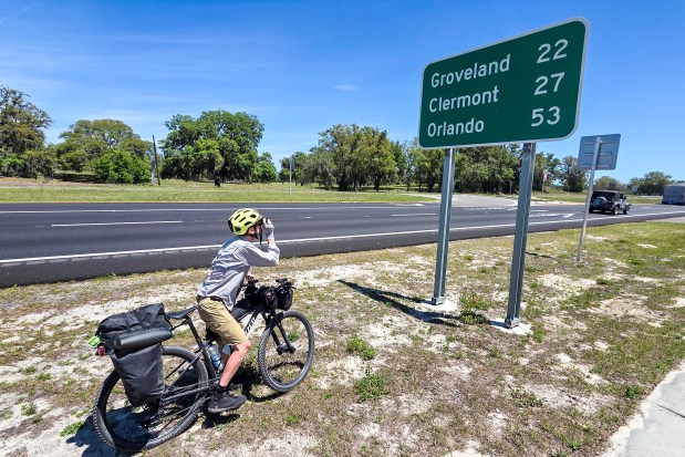 Evan Sanders stops to take a picture of a road sign marking the distance to Groveland, Clermont and Orlando during a four-day bikepacking trip on April 16, 2026. (Patrick Connolly/Orlando Sentinel)