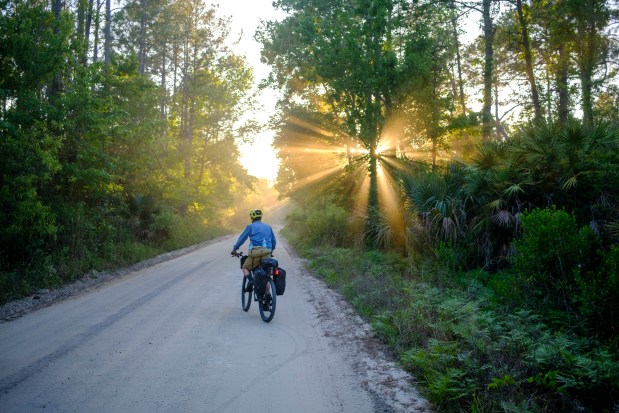 Evan Sanders cycles along a sandy road at sunset while looking for a place to make camp during a four-day bikepacking adventure on April 17, 2026. (Patrick Connolly/Orlando Sentinel)