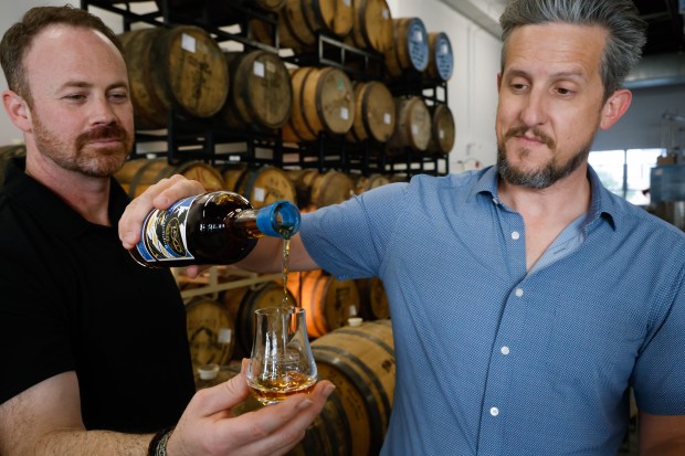 Forward/Slash Distillery owners Tim Bradstreet, left, and Michael Buffa crack a bottle of Ol' Watchdog, the Orlando Sentinel 150th Anniversary whiskey, blended at their Winter Park distillery on Friday, April 24, 2026. (Rich Pope/Orlando Sentinel)
