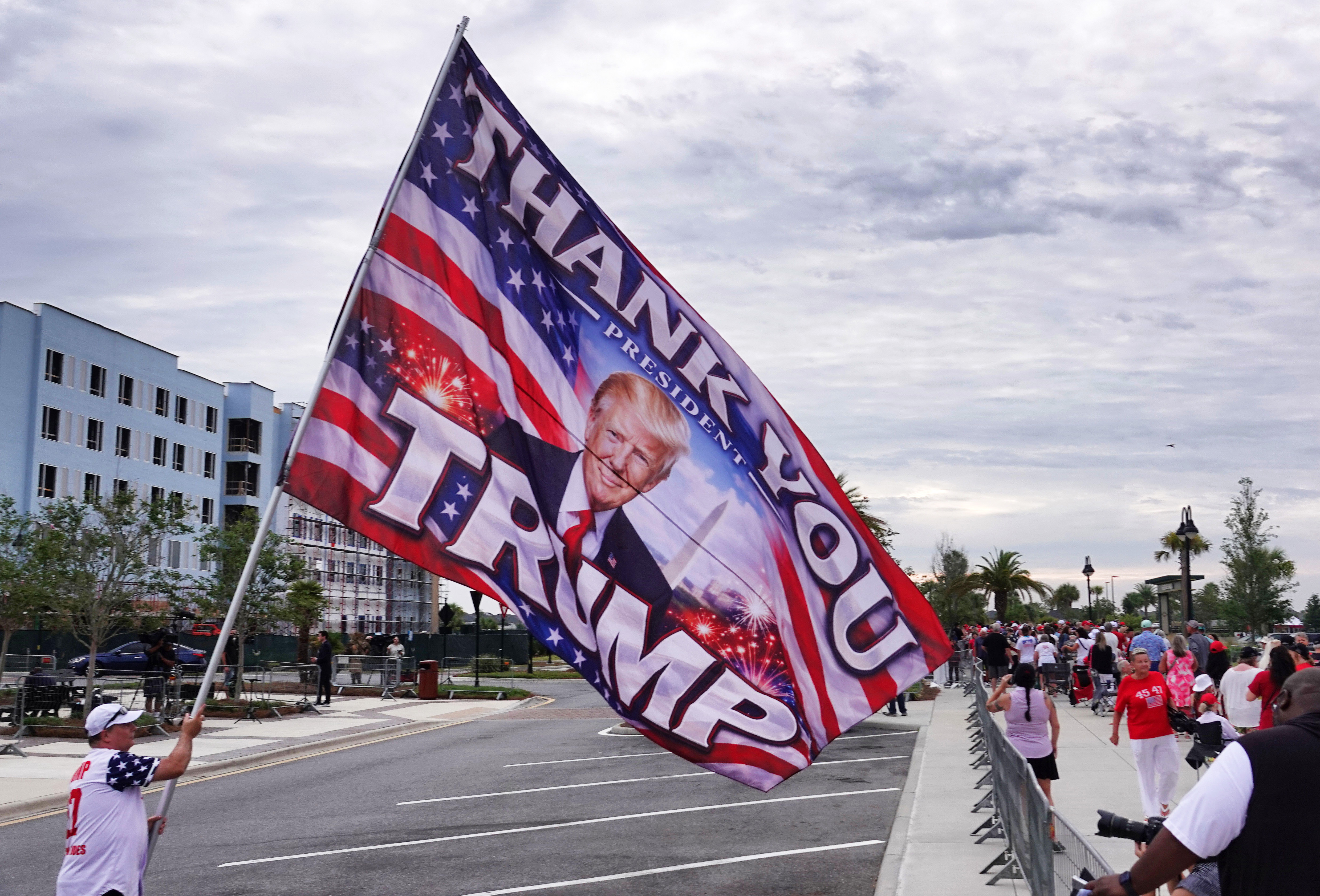A flag-toting fan of President Donald Trump welcomes supporters while...