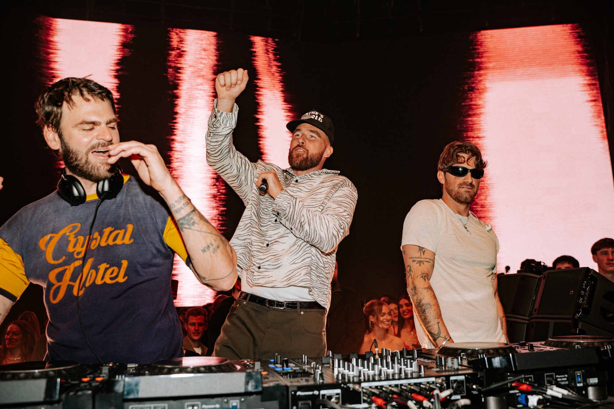 Photo of Travis Kelce and Chainsmokers behind the decks dancing.
