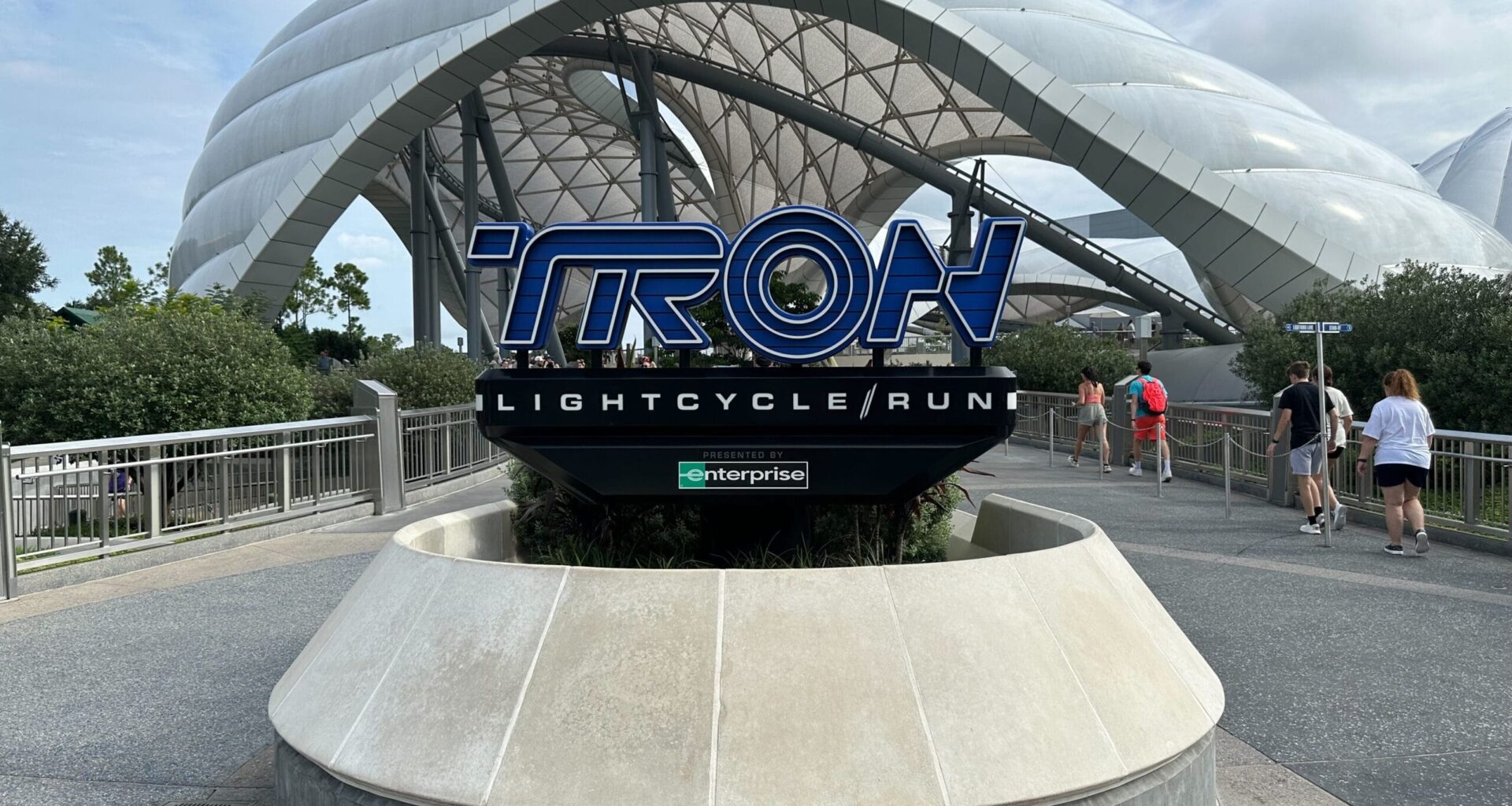 TRON Lightcycle Run sign in front of a sleek, glowing dome, echoing Tomorrowland&rsquo;s energy at Disney Parks, similar to TRON: Ares.