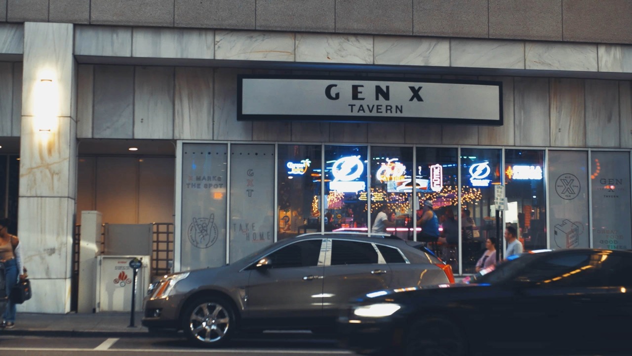 Exterior view of Gen X Tavern in downtown Tampa with illuminated signage and patrons visible inside.