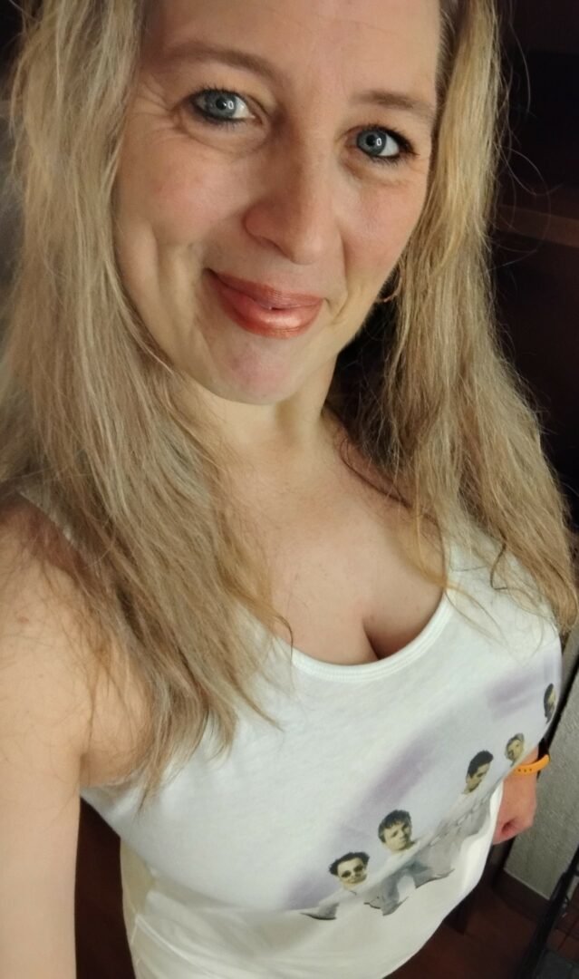 Close-up of a woman with blonde hair smiling, wearing a white shirt with cartoon characters.