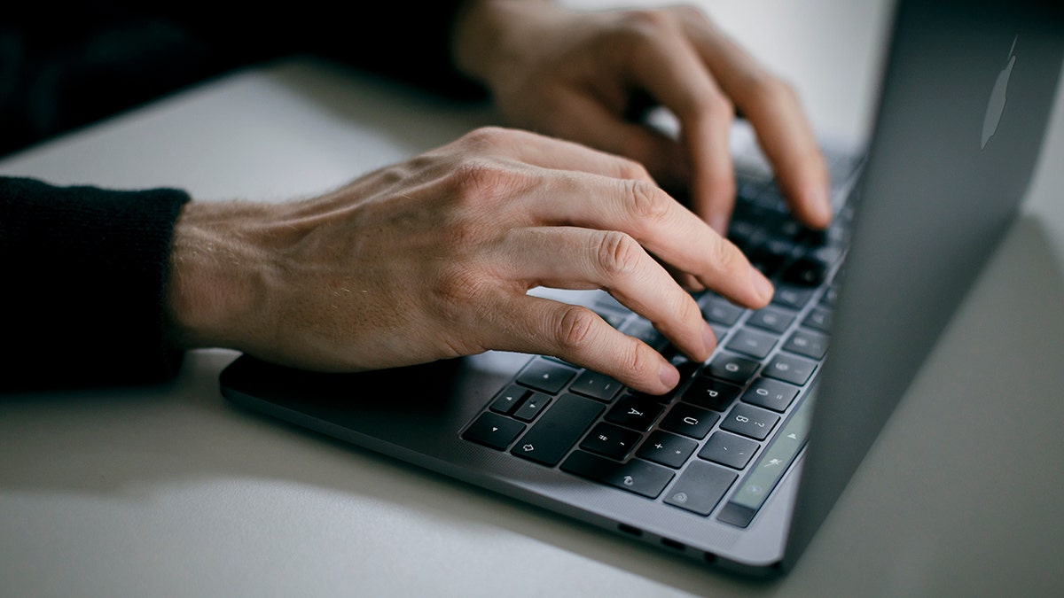 Man typing on laptop keyboard in dim light