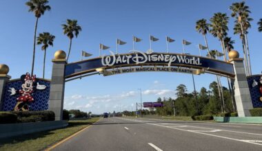 Iconic Walt Disney World entrance arch featuring Minnie and Mickey Mouse, framed by palm trees under a bright blue sky.