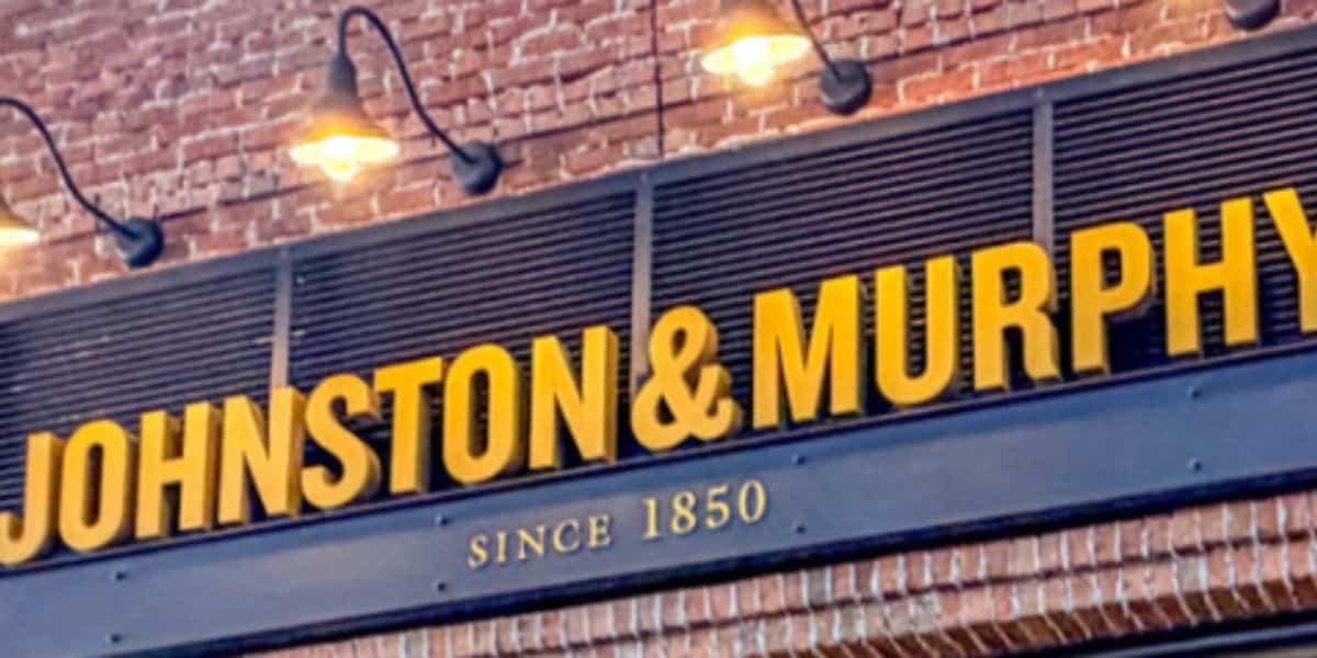 JOHNSTON & MURPHY SINCE 1850 sign atop exposed brick, glowing under marquee lights like a classic Main Street shop.