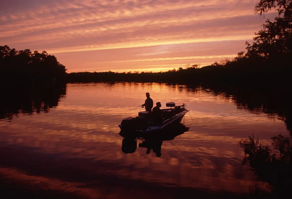 A dramatic sunset colors sky and water, silhouetting a fisherman on Florida's Suwanee River.