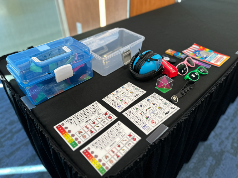 Sensory boxes with contents on a table include communication cards headphones sunglasses and several fidget toys