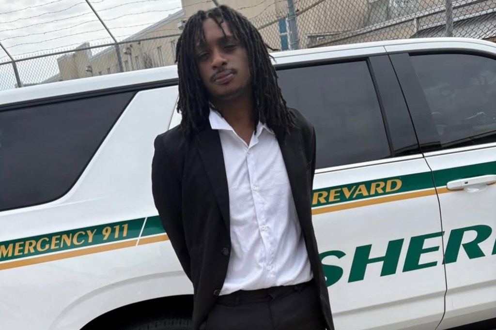 A man in a suit stands in front of a Brevard County Sheriff's vehicle.