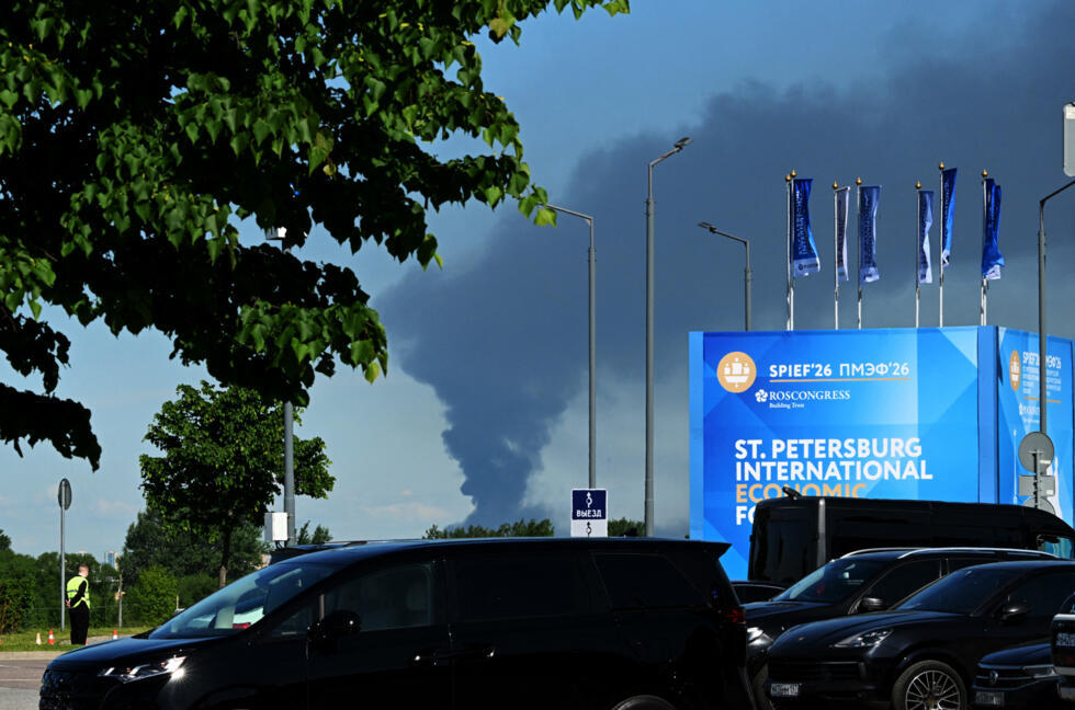 Cars are seen parked near banners with branding for the St. Petersburg International Economic Forum (SPIEF) at the forum's venue as black smoke rises in distance in Saint Petersburg on June 3, 2026.