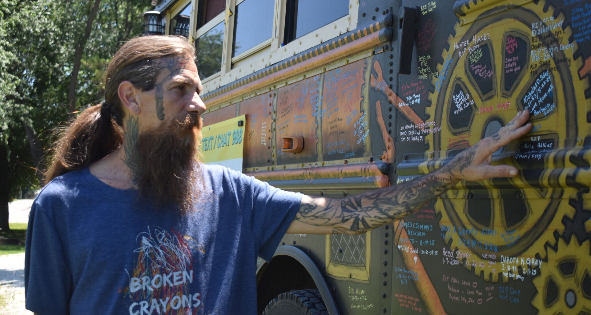 Cory Richez points Tuesday to the side of the Suicide Awareness Bus, where people have written the names of their loved ones who died by suicide. Any glitter on the bus is where ashes were painted onto the vehicle.