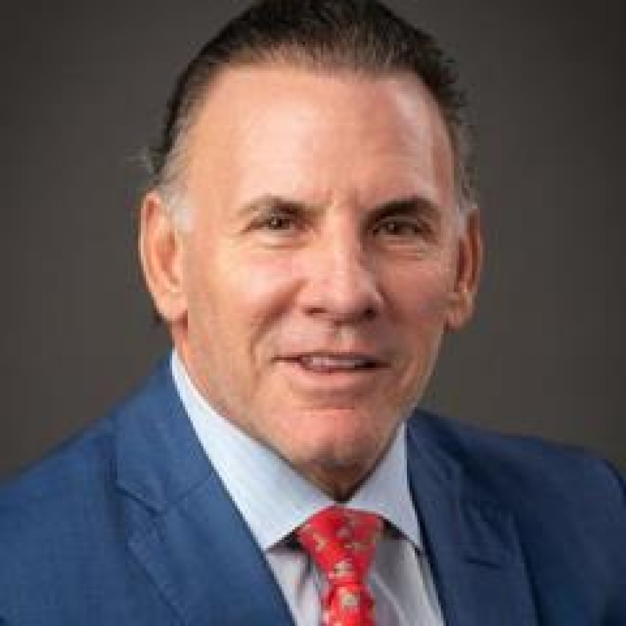 A headshot of a man in a blue suit with a red tie